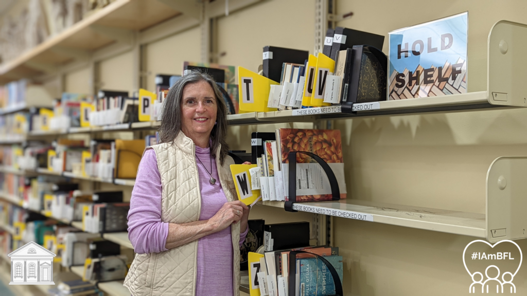 Bernadette smiling in front of our hold shelf