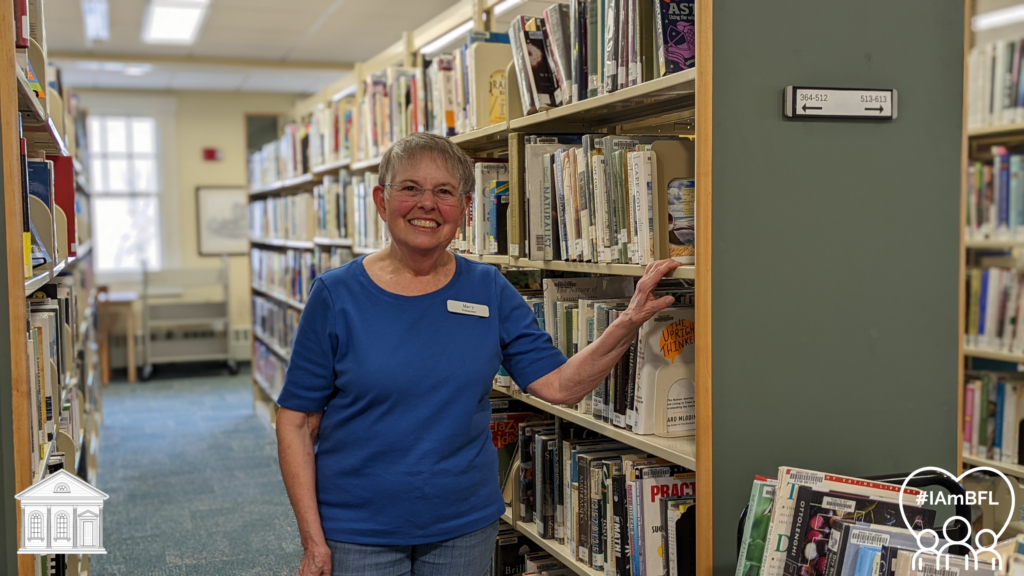 Mary smiling in front of the non-fiction stacks