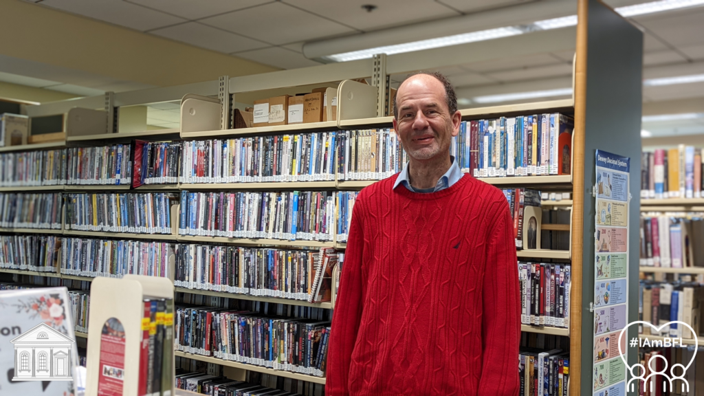 Mark smiling in front of the Non-Fiction DVDs