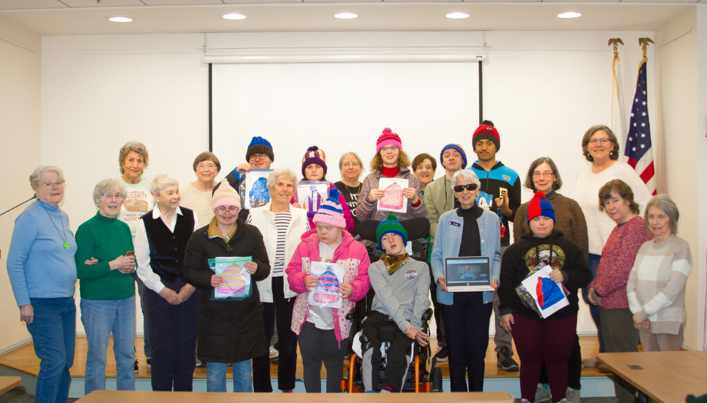 SHORE students are wearing hats and holding their hat designs standing with the knit lit members who knitted their hats. Students chose a range of colors and designs in blue, green, pink, orange and red.