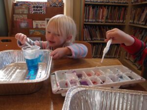 Blond preschool girl uses an eyedropper to add color to a cup of water